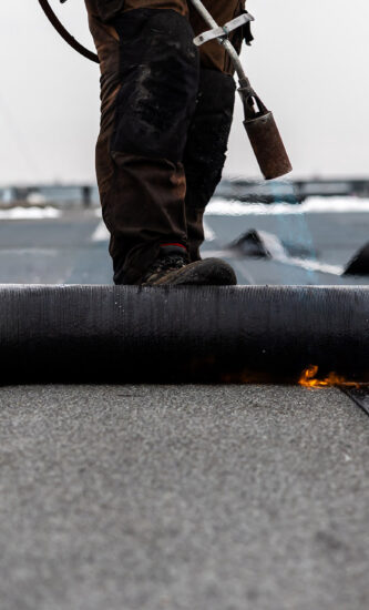 professional roofer at work securing rolled tar paper with a blowtorch on a flat roof installation process professional roofer at work securing rolled tar paper with a blowtorch on a flat roof installation process